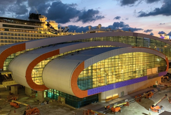 Construction work lights shine through the glass walls of Norwegian Cruise Lines Port of Miami Terminal at dusk
