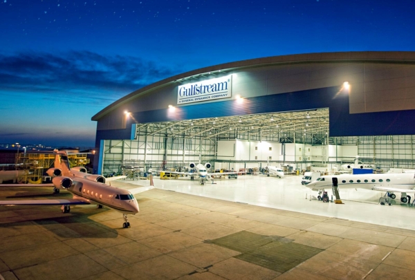 Exterior of Gulf Stream Service Center at night. Planes inside hangar and outside on apron.