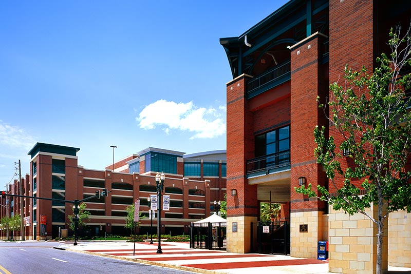 Exterior photo of Jacksonville Municipal Garages. Photo is a view from the street of the sports arena parking garage. Trees line the street. Red brick with green trim accent the garage.