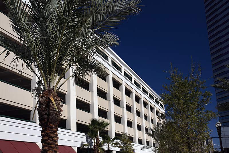 Exterior photo of the City of Jacksonville parking garage. Close up photo of the side. Palm tree and another tree frame the photo.
