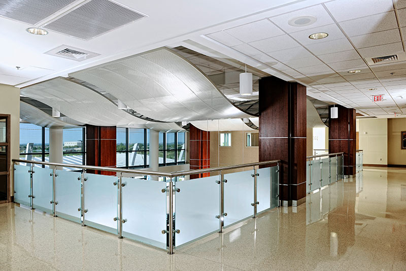 Interior photo from inside St John Broken Arrow. Wave like structures hang form the ceiling. Frosted glass and metal railing surround the overlook.