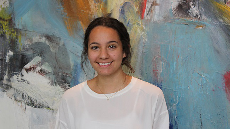 Haskell intern Camila Moreno smiling in front of colorful artwork.
