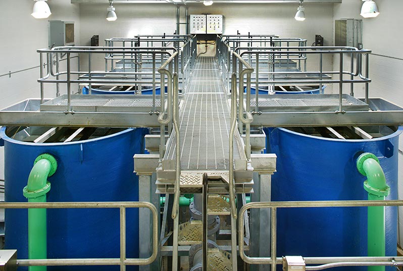 Aluminum grating walkways above six large blue tanks with green piping at the Indian Head Wastewater Treatment Plant.
