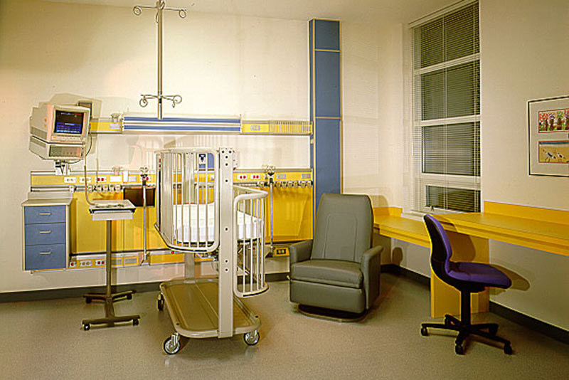 Interior photo of hospital room. Crib bed and chair sit in the middle of the room.
