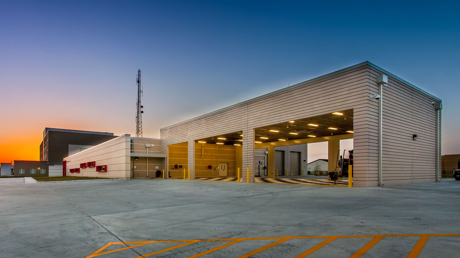 MSST Houston exterior at dusk|Nighttime photo of MSST Houston building entry|K-9 in fenced enclosure|Locker Room with bright blue lockers and grey tile surfaces|Fenced K-9 training yard with obstacle course and shade canopy|MSST Houston interior|Boat maintenance bay|Building exterior featuring bright red metal panel window cowlings|MSST Houston entry doors and freestanding sign|Boat storage bay|MSST Houston nighttime exterior|MSST Houston exterior|MSST Houston building exterior|||||||||||||