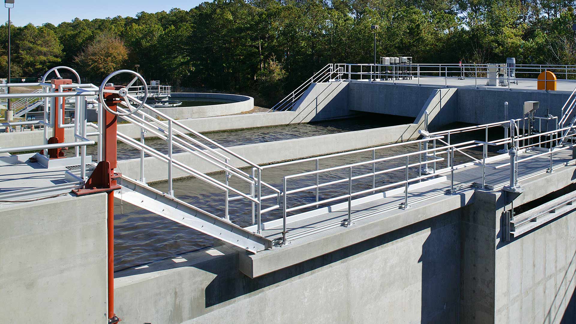 Large concrete water storage containers at Glynn County Water Pollution Control Plant|Exterior photo of the brick/stone facility|Large concrete wastewater processing tanks|Interior photo of water testing room|Solids conveyor system and water pipes inside the facility|Aerial photo of Glynn County Water Pollution Control Plant||||||