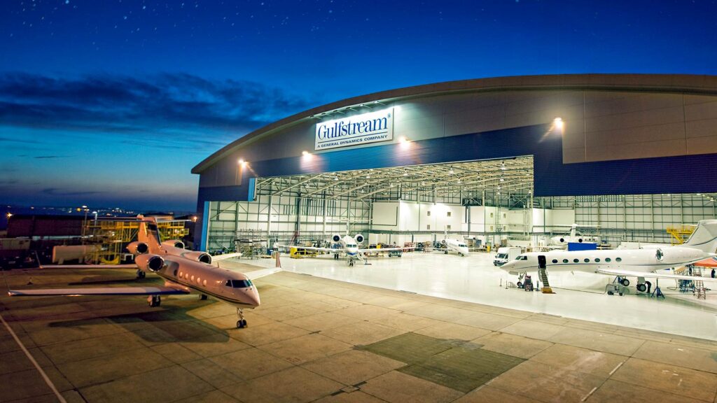 Exterior of Gulf Stream Service Center at night. Planes inside hangar and outside on apron.|