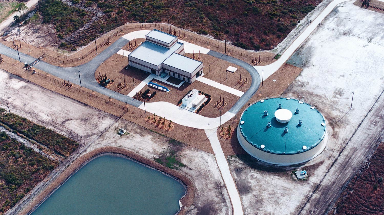 Aerial photo of Cecil Commerce Center Water Treatment Plant|Aerial photo of Cecil Commerce Center Water Treatment Plant|Exterior photo of the brick facility housing vertical tanks.|Interior photo from inside the facility. Large blue pipes and valves.||||
