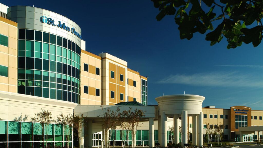 Exterior photo of Owasso Hospital and Medical Office Building. Four-story hospital entrance against bright blue skies.