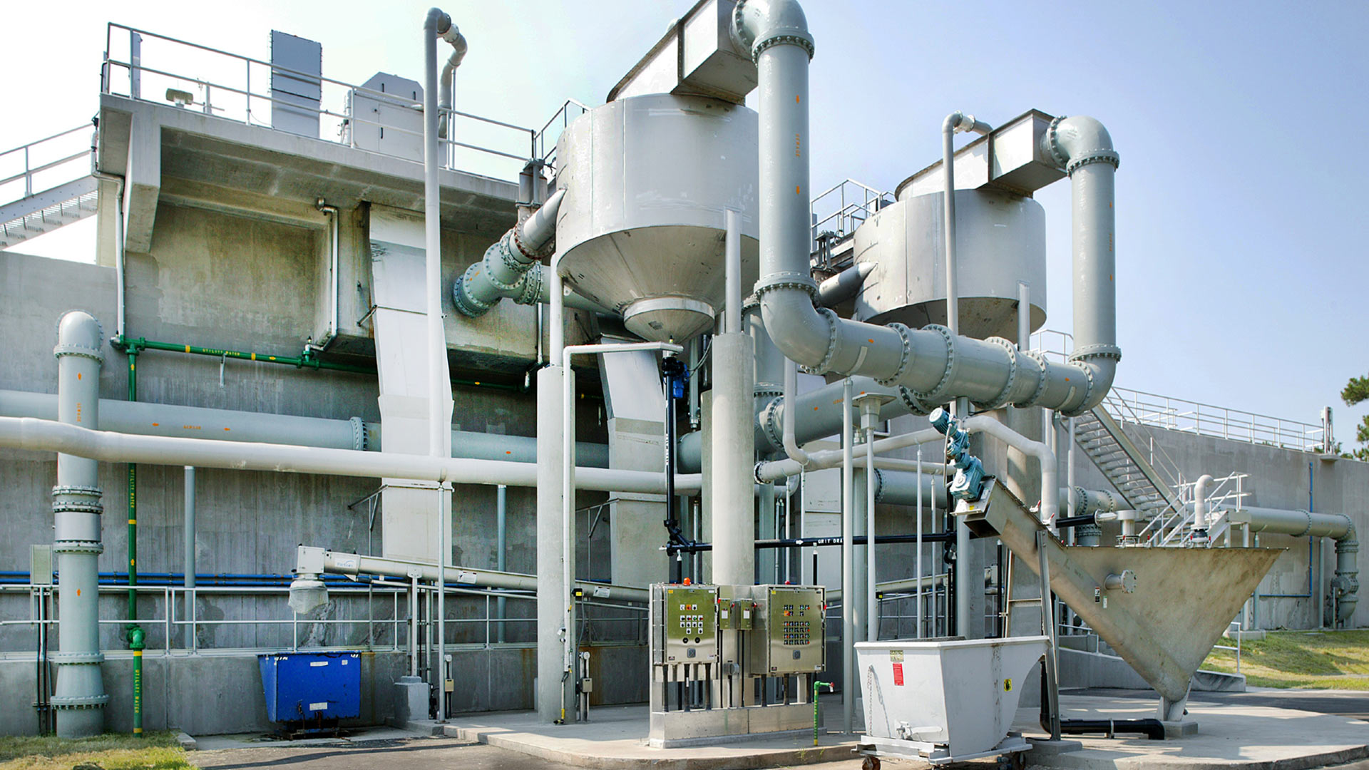 Metal pipes and other water distribution equipment at the Point Peter Wastewater Treatment Plant|Exterior photo of green and white facility|A crane lifts a beam across a swampy grassy marsh.|Aerial photo during construction of the Point Peter Wastewater Treatment Plant|Aerial photo of the Point Peter Wastewater Treatment Plant|||||