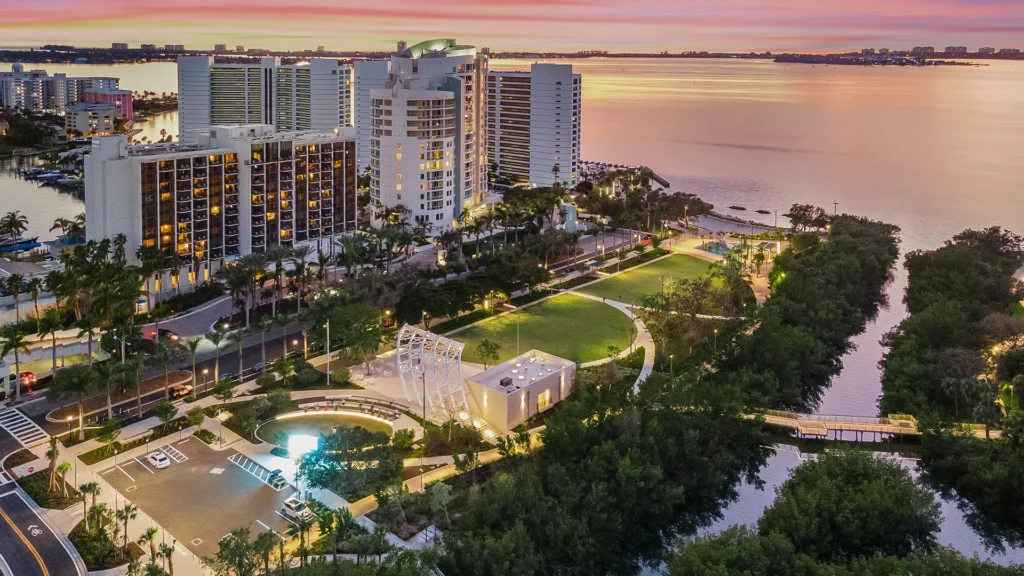 Aerial view of The Bay waterfront park in Sarasota with lawns, pathways, high-rise buildings and Sarasota Bay at sunset.