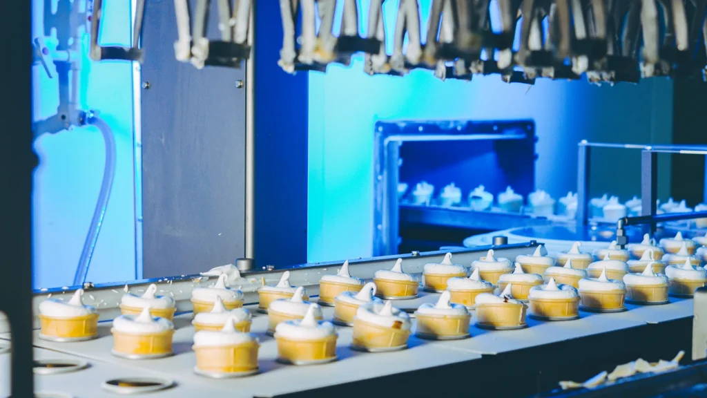 Individual ice cream cups topped with soft-serve swirls move along an automated production line.