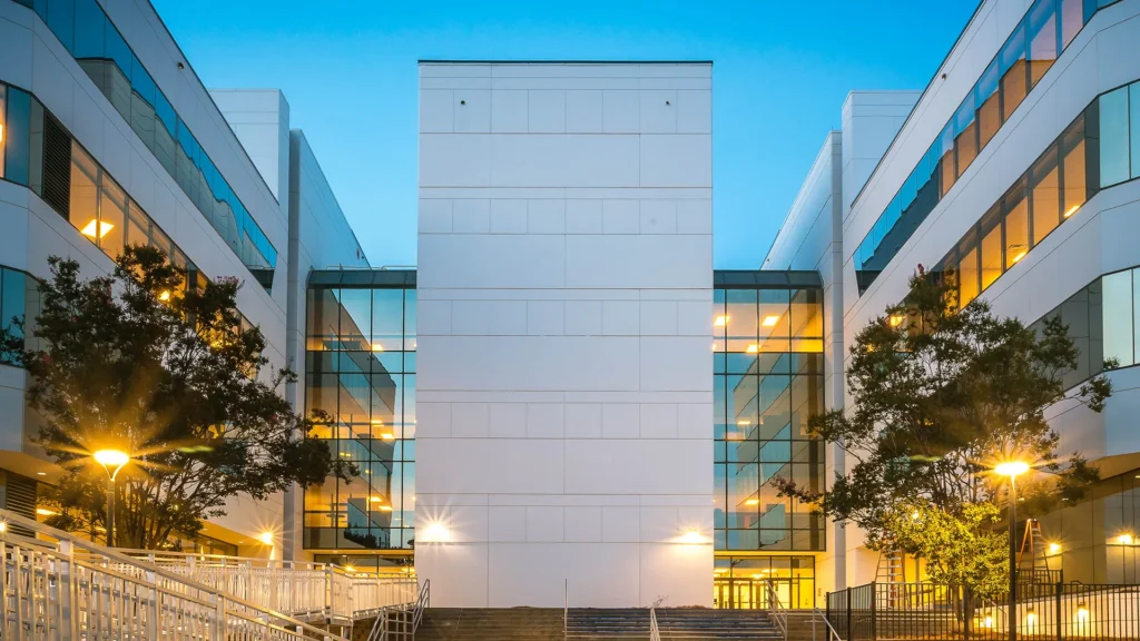 American Leadership Academy Blythewood exterior with white façades, glass walls and illuminated walkways at dusk.