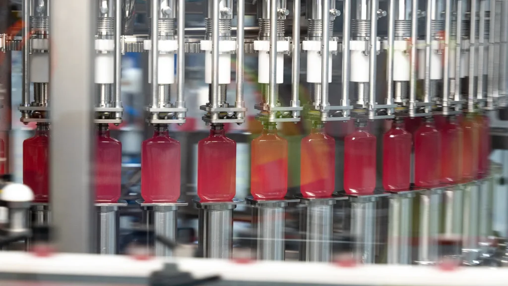 Red flask bottles move through automated filling equipment on a high-speed production line.