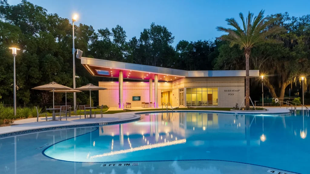 Jacksonville University’s River House Pool complex illuminated at dusk, with a modern pool house, palm trees and outdoor seating.
