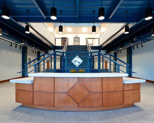 Wood paneled reception desk in front of bifurcated blue stairway