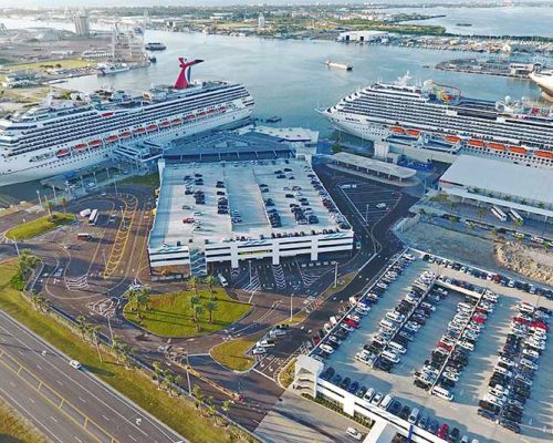 Aerial photo of Canaveral Port Authority Cruise Terminal 5. Two cruise ships in port. One of the ships is docked at the new two-story passenger and baggage handling areas. Large parking garages.