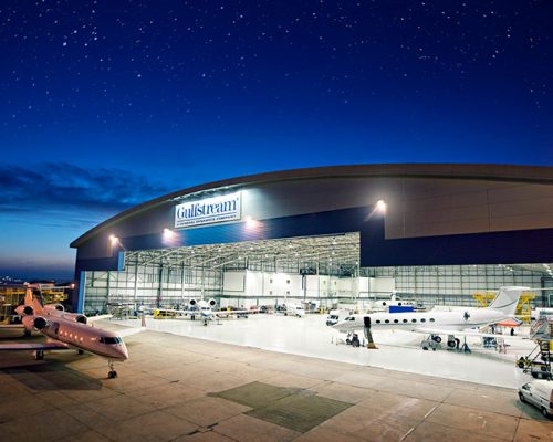 Exterior of Gulfstream International Service Facility at night with planes within the hangar.