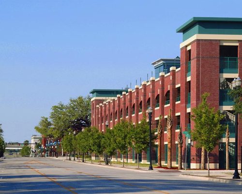 Exterior photo of Jacksonville Municipal Garages. Photo is a streetscape view of the parking garage with a church steeple in the background. Trees line the street. Red brick with green trim accent the garage.