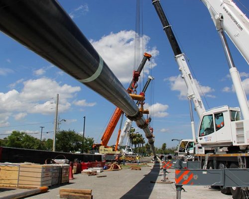 Large black pipe suspended from crane at jobsite.