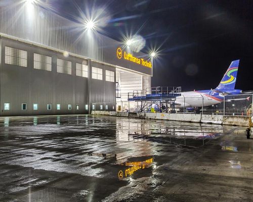 Exterior of Lufthansa Technik Heavy Maintenance Facility at night. Airplane entering hangar in the back.