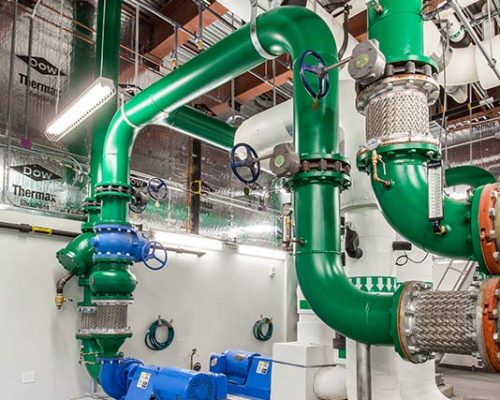 Photo from inside the central energy plant with green piping and blue pumps.