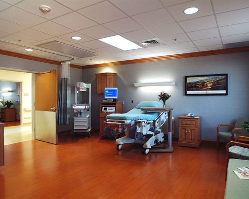Interior photo of large hospital bedroom. Wood floors and cool grey walls.