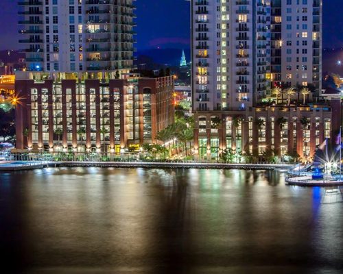 Photo of Jacksonville's Southbank Riverwalk at night from across the river. Building lights reflect off the water.