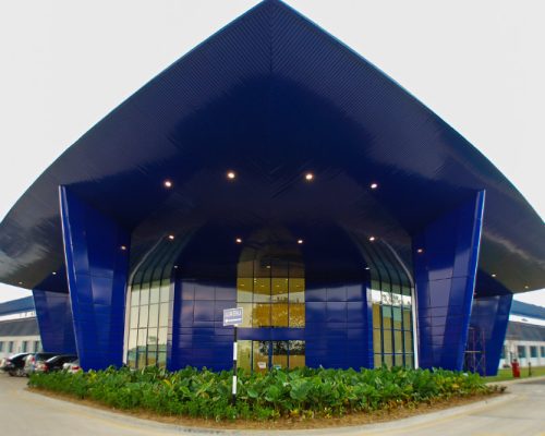 Exterior entrance of Spirit AeroSystems SE Asia. Bright blue triangular building.
