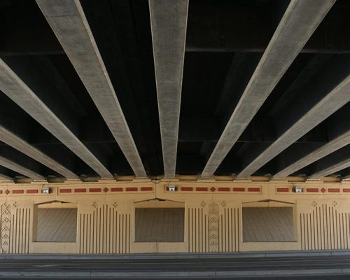 View of bridge piers and decking from beneath highway overpass