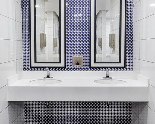 Restroom vanity with dual sinks and mirrors. White, blue and dark gray tile surfaces.