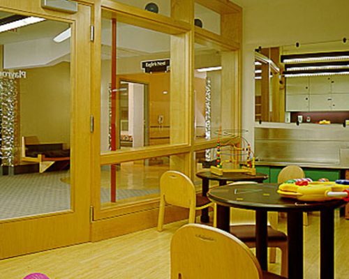 Interior photo of children's play area. Glass windows and door separate room from hallway