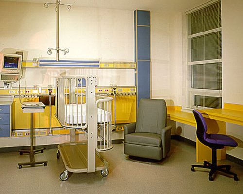 Interior photo of hospital room. Crib bed and chair sit in the middle of the room.